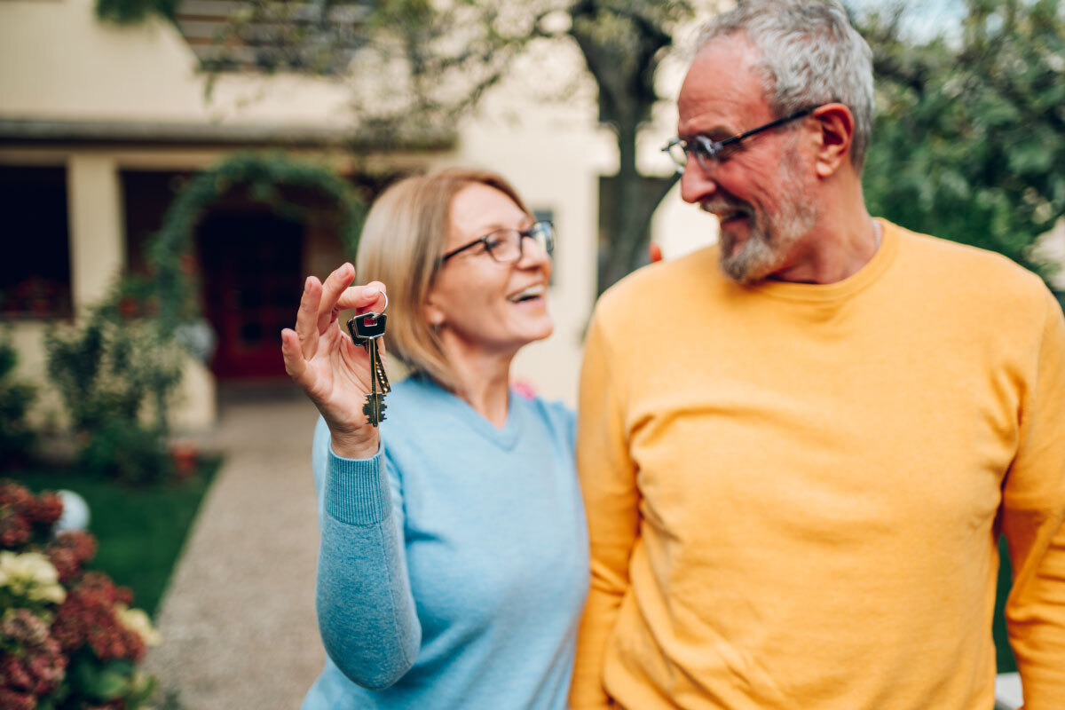 pareja-ancianos-con-llaves-en-mano-y-de-pie-delante-de-casa